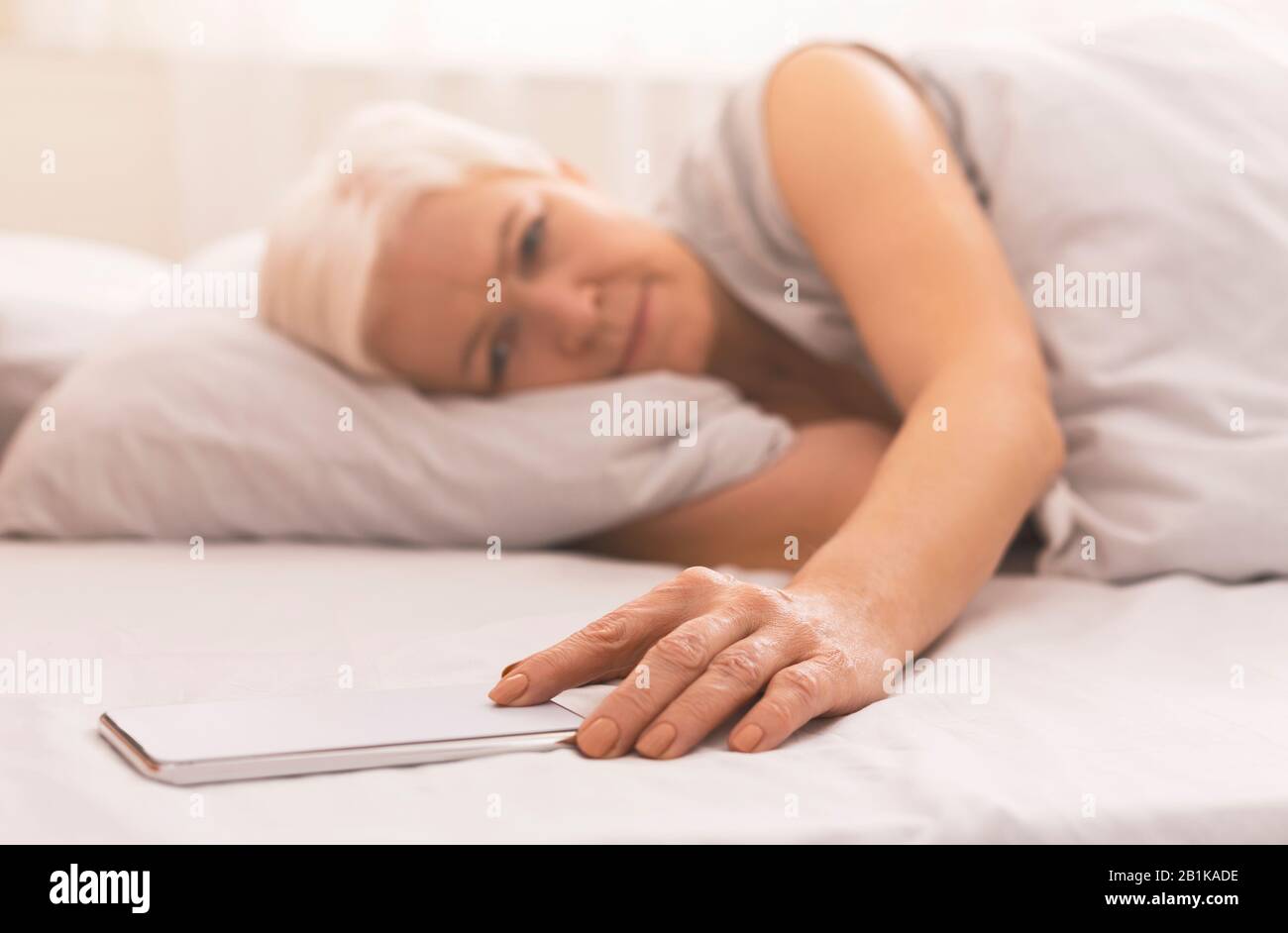 Donna anziana stanco nel tempo di controllo del letto sul suo telefono Foto Stock