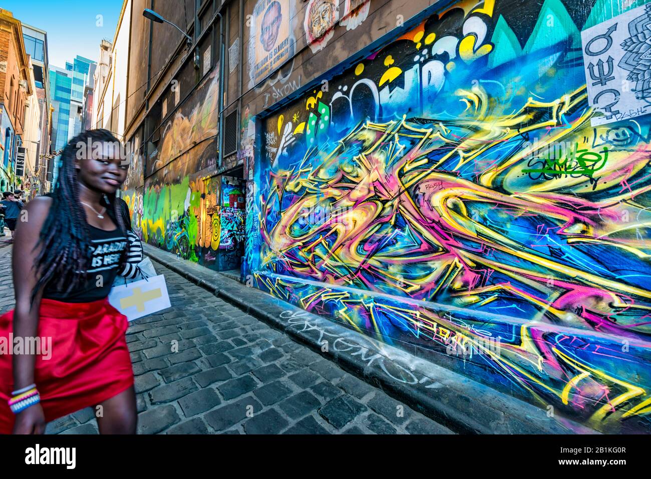 Giovane donna nera alla moda con minigonna rossa, trecce nere, camminando lungo strade acciottolate, Hosier Street, Melbourne Lanes, Melbourne, Victoria, Foto Stock