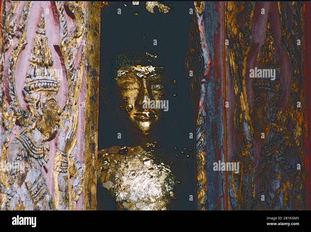 Immagine di Buddha in bronzo con foglia d'oro dietro pannelli di legno intagliati in modo intricato in un tempio tailandese. Foto Stock