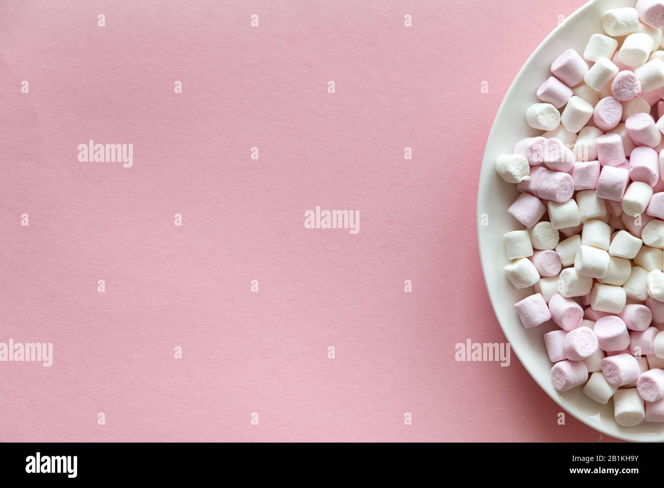 Mini marshmallow rosa e bianco in piastra bianca su sfondo rosa con spazio libero per il testo Foto Stock