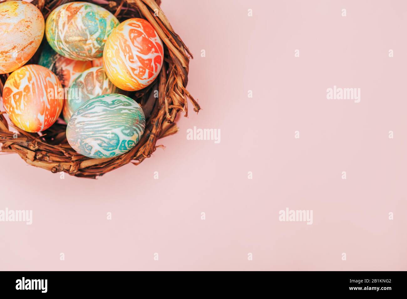 Le uova di pasqua Coloseful nel nido su sfondo di colore rosa pastello. Foto Stock