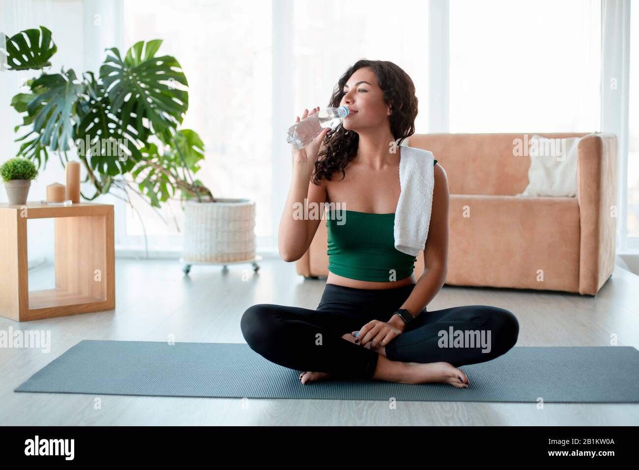 Giovane donna ispanica che beve acqua sul tappetino yoga a casa Foto Stock
