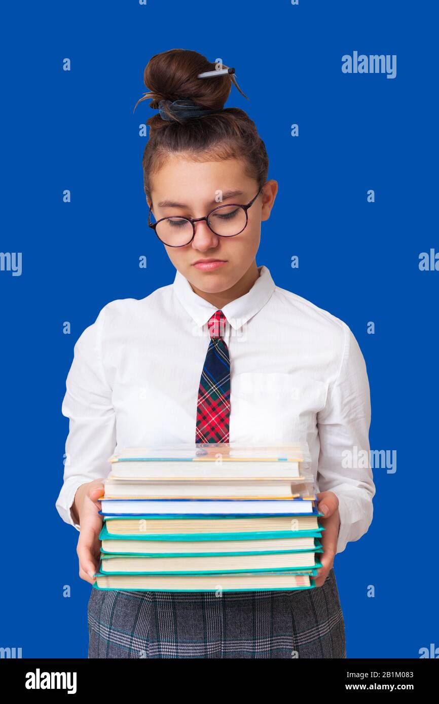 scolaretta tiene libri nelle sue mani e sembra dispiaciuto. non vuole studiare. isolato su sfondo blu Foto Stock