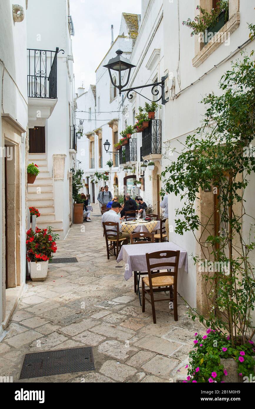 Tavoli fuori ristorante nella stretta strada pedonale, Locorotondo, Puglia, Italia Foto Stock