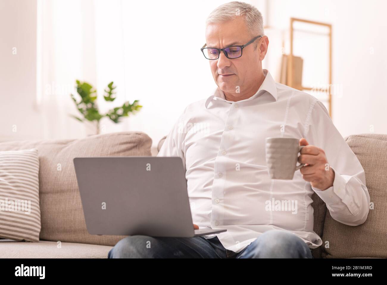 Uomo Anziano Che Usa Il Laptop E Ha Tè Foto Stock