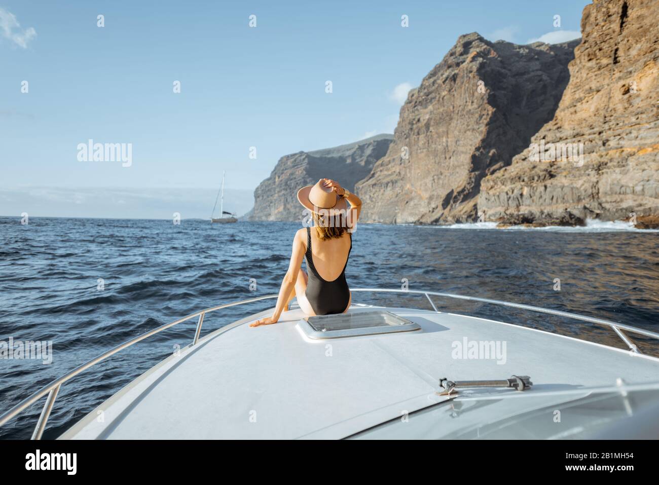 Donna che gode di un viaggio in oceano seduto sul naso dello yacht mentre naviga vicino alla costa rocciosa mozzafiato su un tramonto Foto Stock