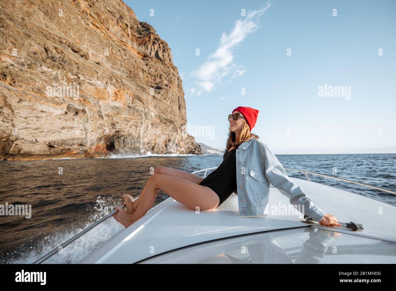 Donna vestita casualmente godendo viaggio oceanico, navigando su uno yacht vicino alla costa rocciosa mozzafiato su un tramonto. Concetto di uno stile di vita e di viaggio spensierati Foto Stock