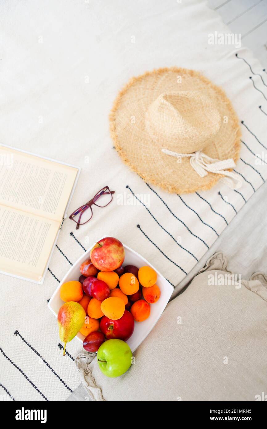 Vista dall'alto del libro aperto con bicchieri e piatto di deliziosa frutta colorata con cappello di paglia sul letto del resort Foto Stock