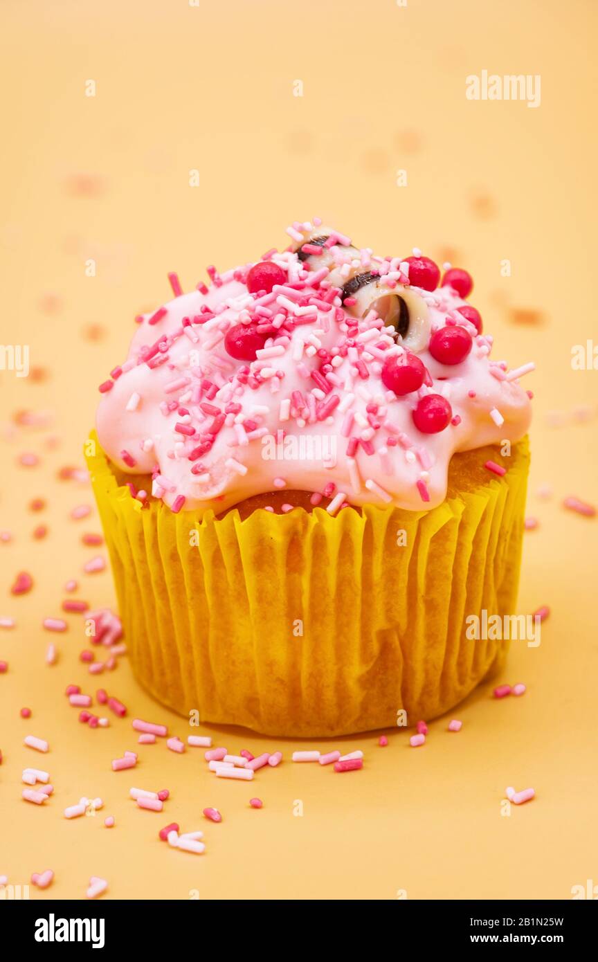 Decorazione di un Cupcake con Sprinkles su sfondo pastello arancione. Foto Stock