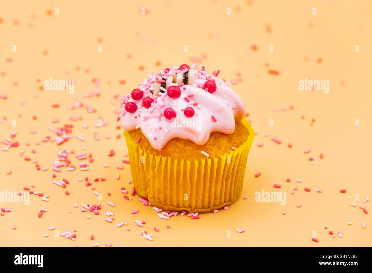 Decorazione di un Cupcake con Sprinkles su sfondo pastello arancione. Foto Stock