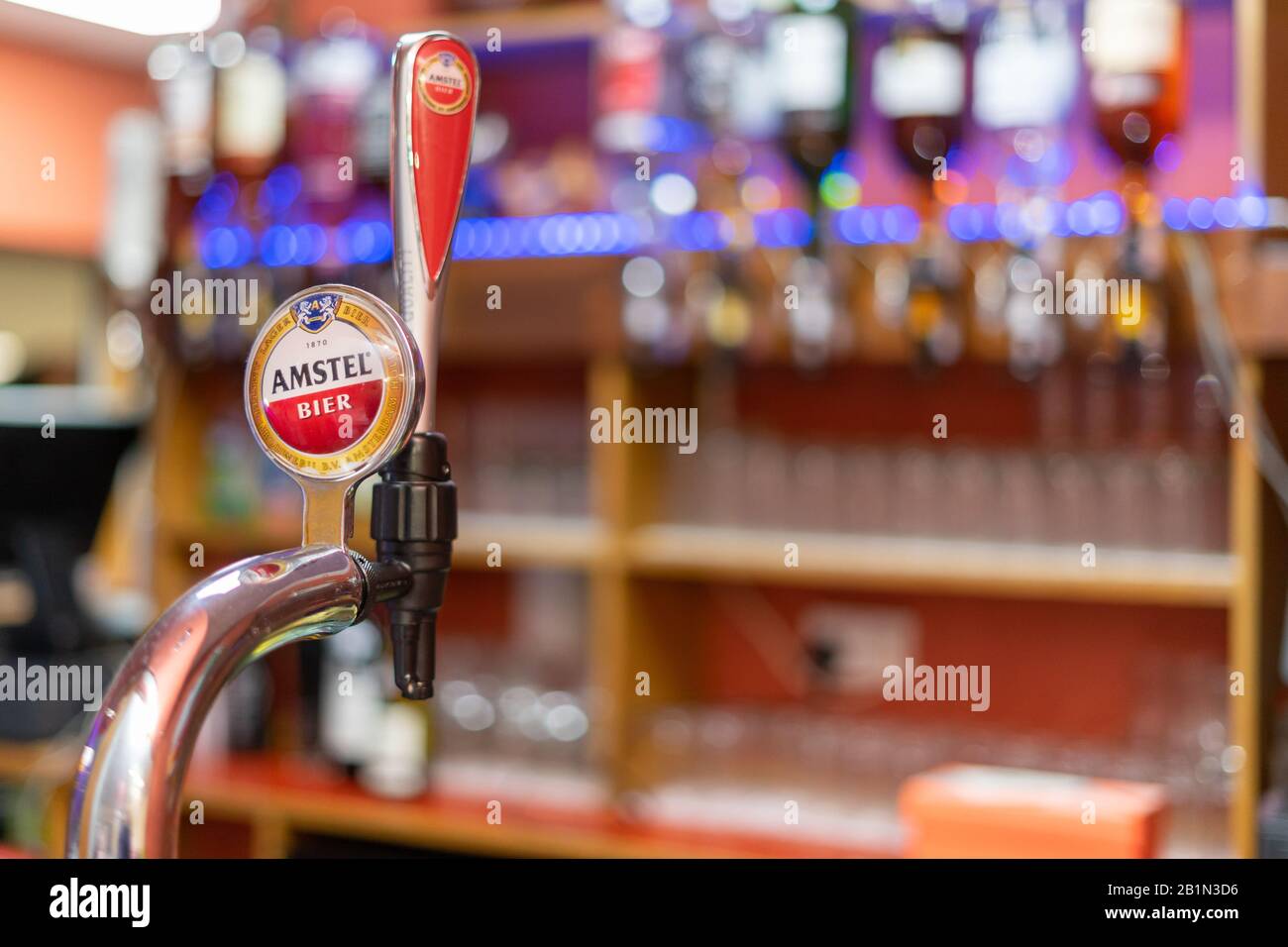 Una birra Amstel pompa su un bar in un pub con ottica e bicchieri sullo sfondo Foto Stock