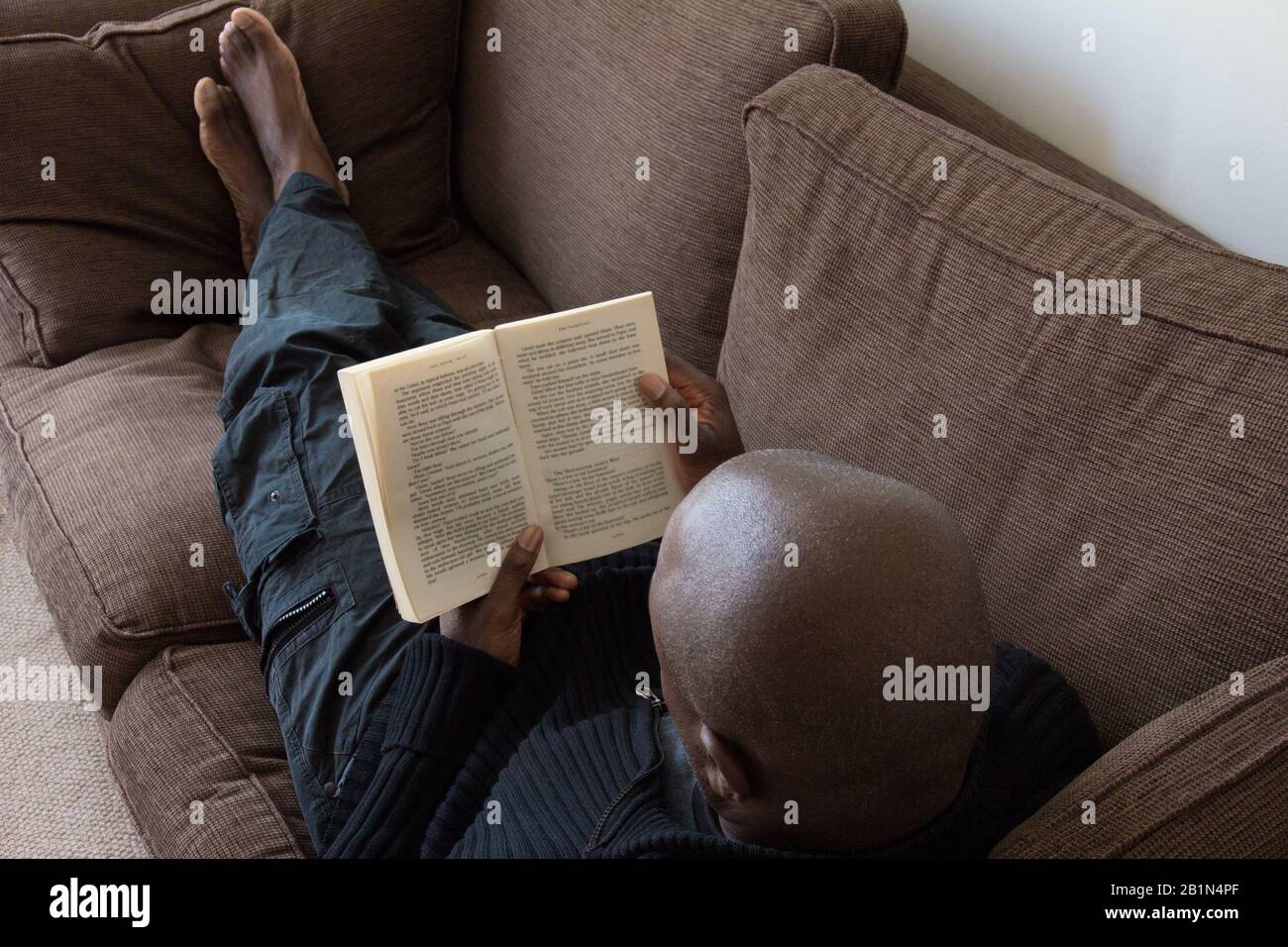 Uomo nero, di etnia africana, leggendo sul divano a casa Foto Stock