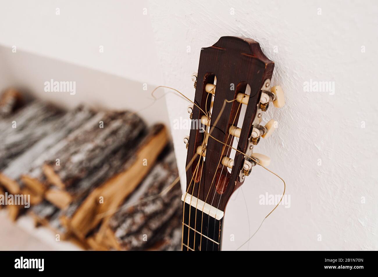 Collo e testa del collo della chitarra acustica con archi stracciati da vicino. Focolare artificiale sfocato e un log per un fuoco Foto Stock