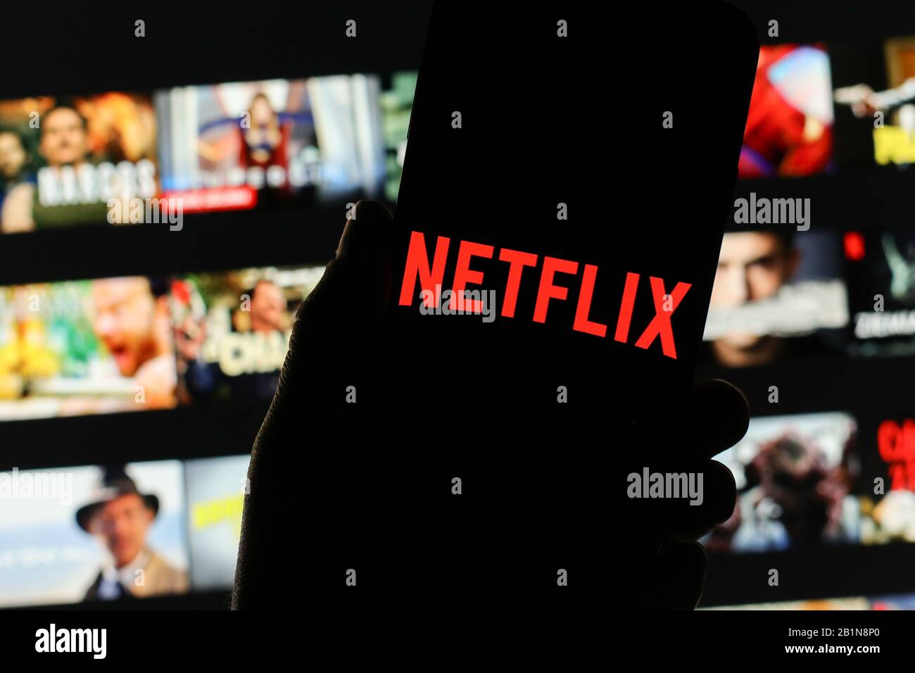 Il logo Netflix dell'azienda viene visualizzato sullo schermo dello smartphone con lo schermo di benvenuto Netflix visibile sfocato sullo sfondo Foto Stock
