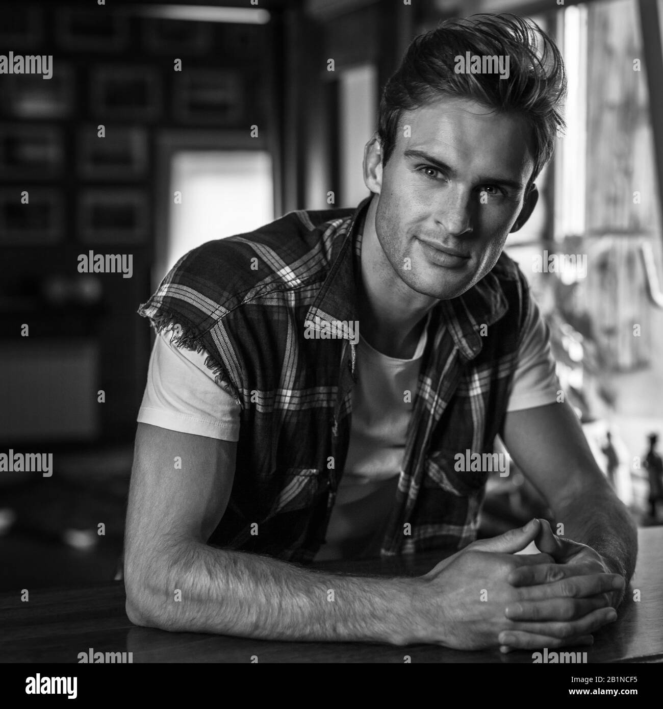 Bel giovane uomo in abiti casual posa contro casa interiore. Ritratto bianco-nero Foto Stock