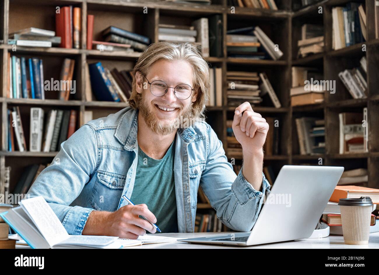 Ritratto giovane studente a casa biblioteca scrivania prendere appunti da manuale portatile. Foto Stock