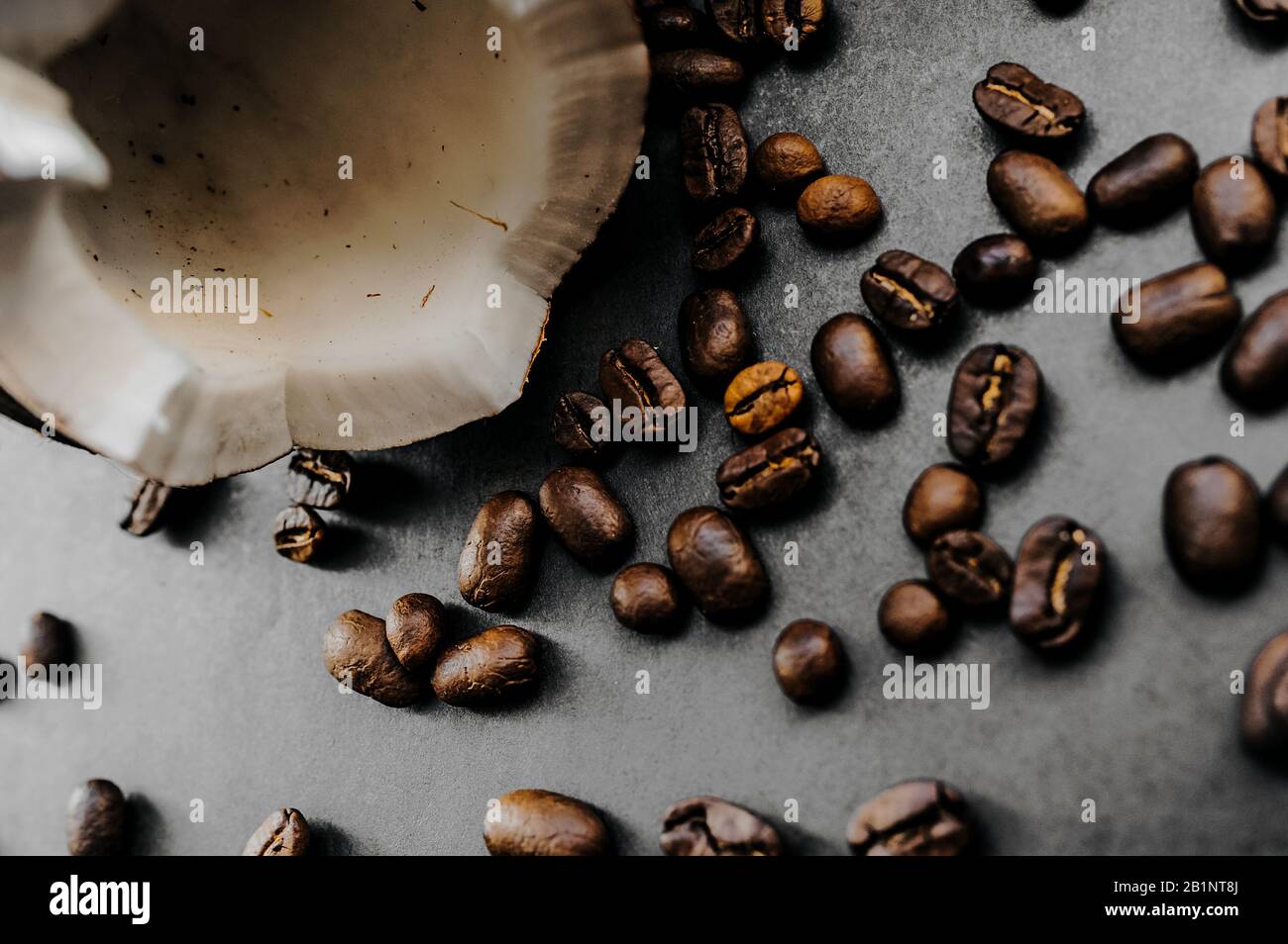 grani scuri fritti sparsi di caffè arabica e cocco rotto maturo su uno sfondo uniforme nello stile di nero totale minimale Foto Stock