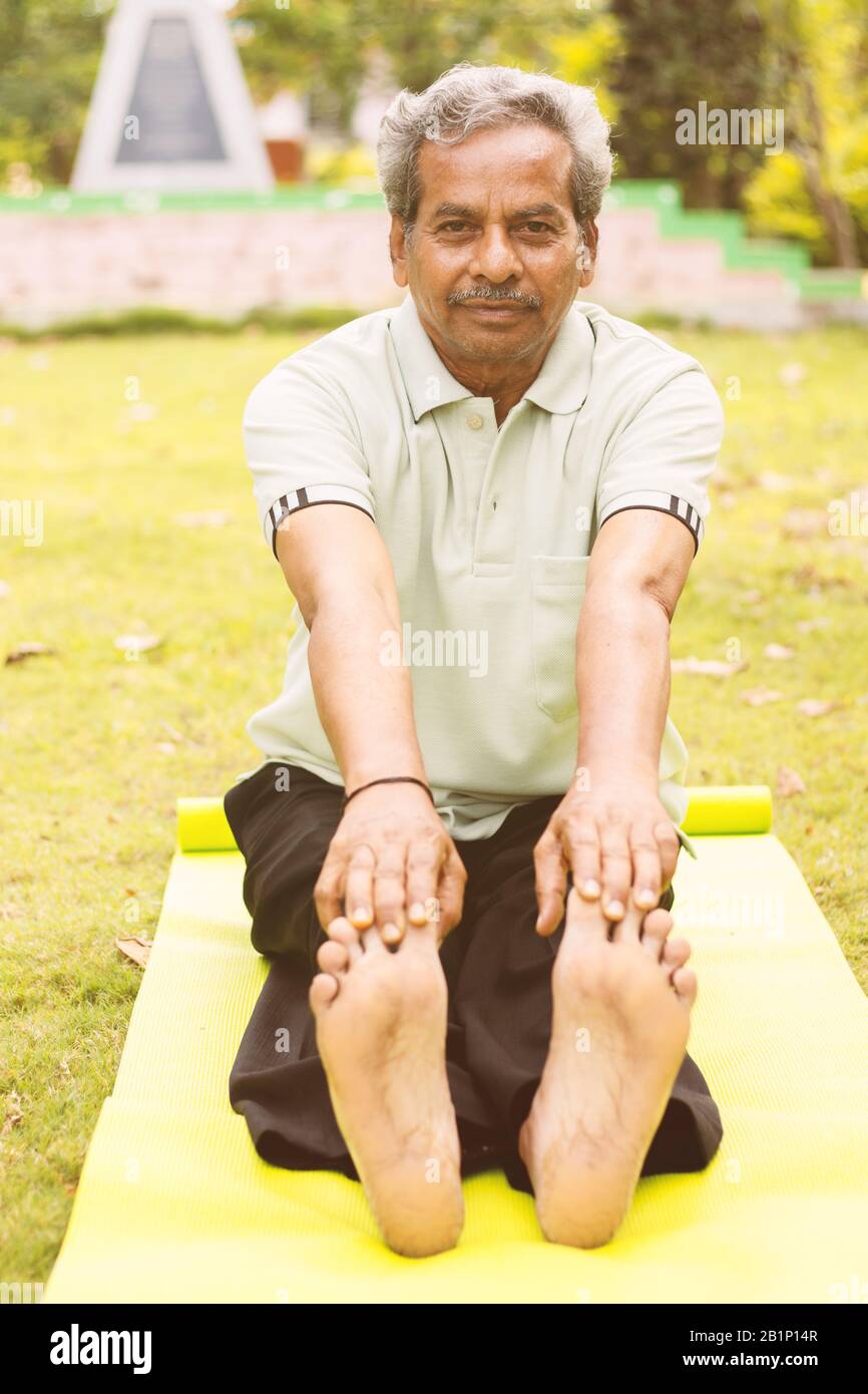Vista a tutta lunghezza e basso angolo di un vecchio uomo seduto in giù per l'esercizio o stuoia di yoga che tocca le dita dei piedi - Concetto di salute e fitness attivi e felici anziani Foto Stock