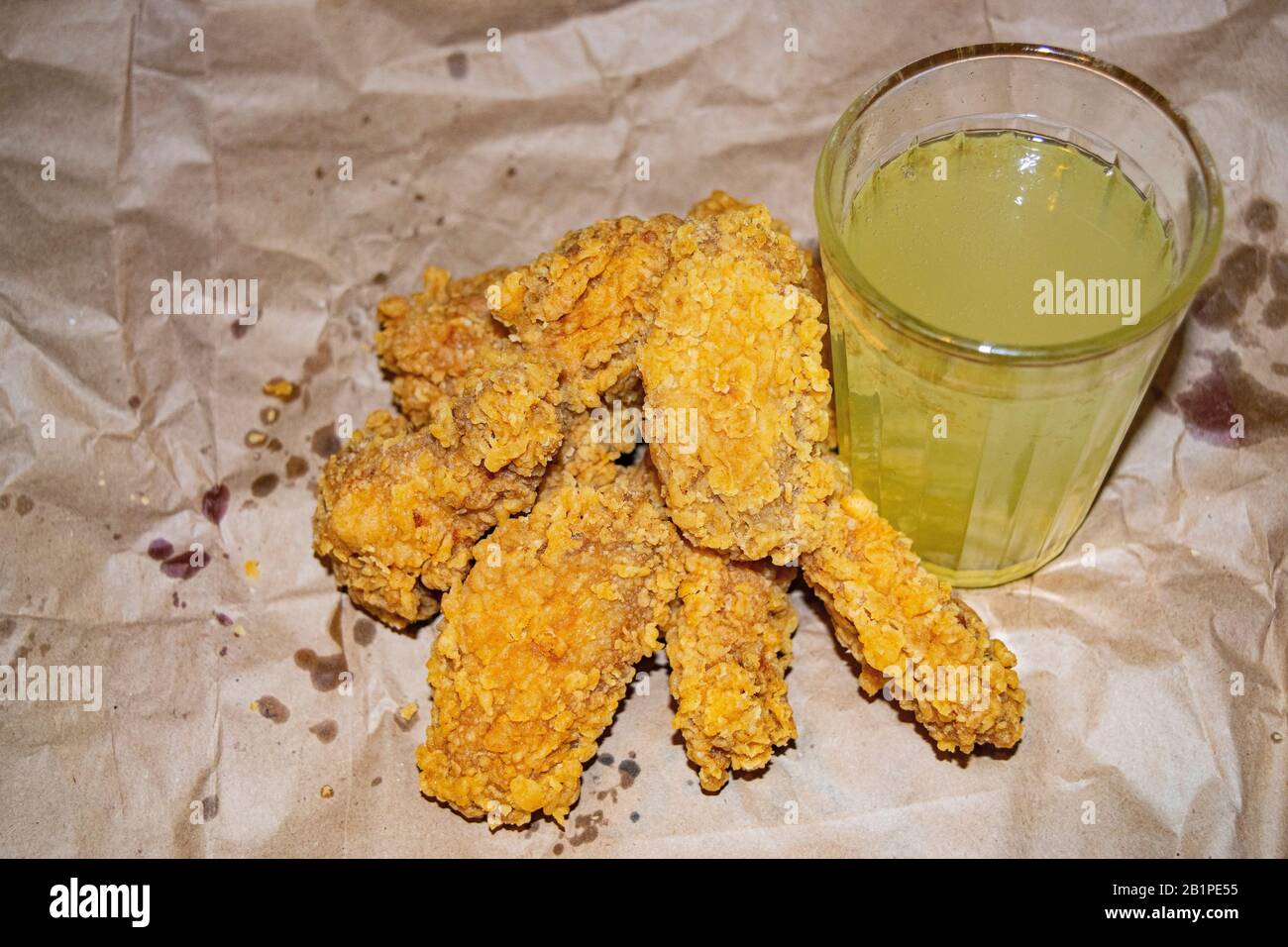 Ali di pollo impanate e un bicchiere di limonata su sfondo grigio di carta. Primo piano Foto Stock