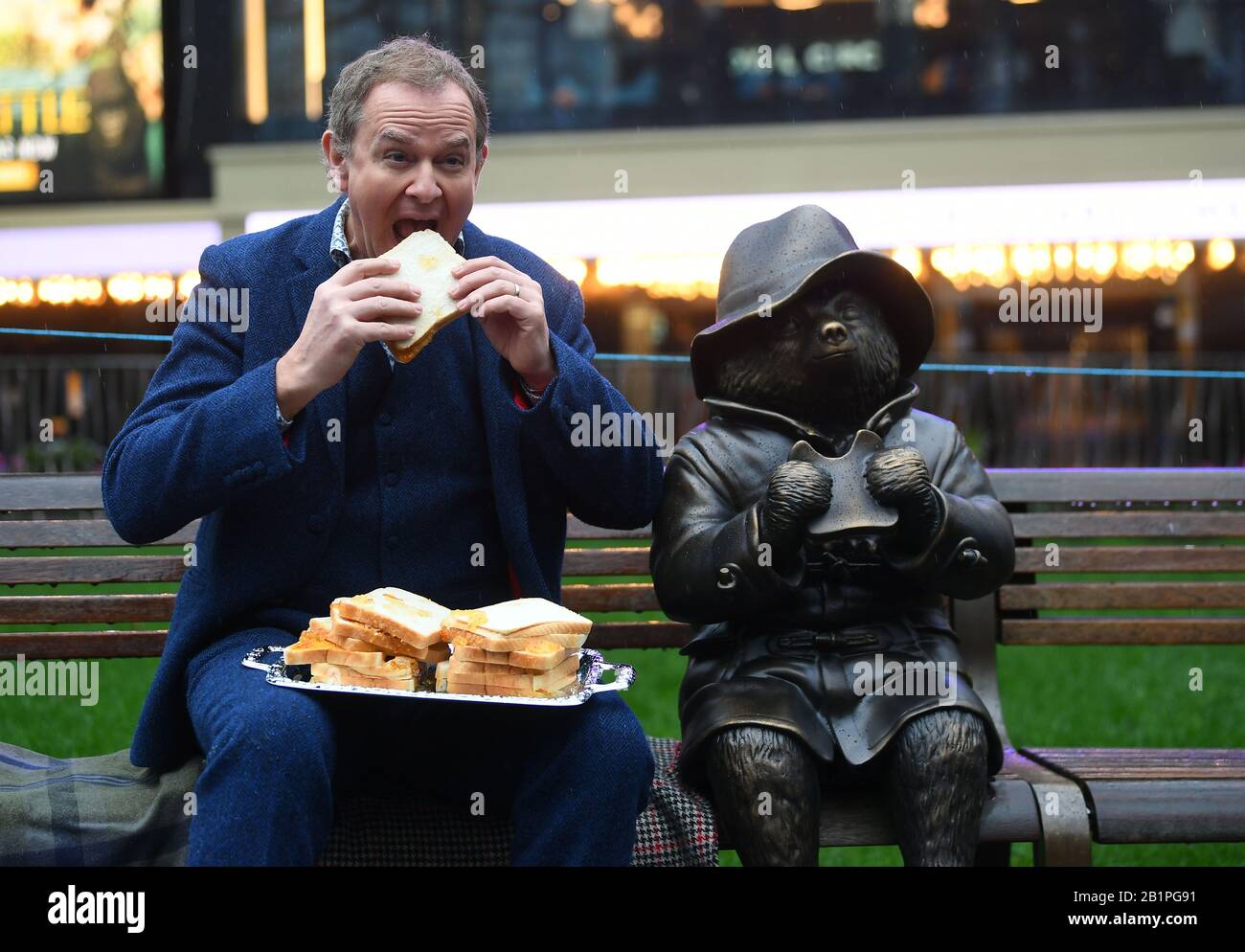 Hugh Bonneville mangiando un sandwich di marmellata accanto ad una statua dell'Orso di Paddington mentre assiste Le Scene Del percorso della statua di Square, svelando a Leicester Square, Londra. Foto PA. Data Immagine: Giovedì 27 Febbraio 2020. Otto statue saranno svelate per segnare il valore di un secolo di cinema in Piazza. Il credito fotografico dovrebbe essere: Victoria Jones/PA Wire Foto Stock