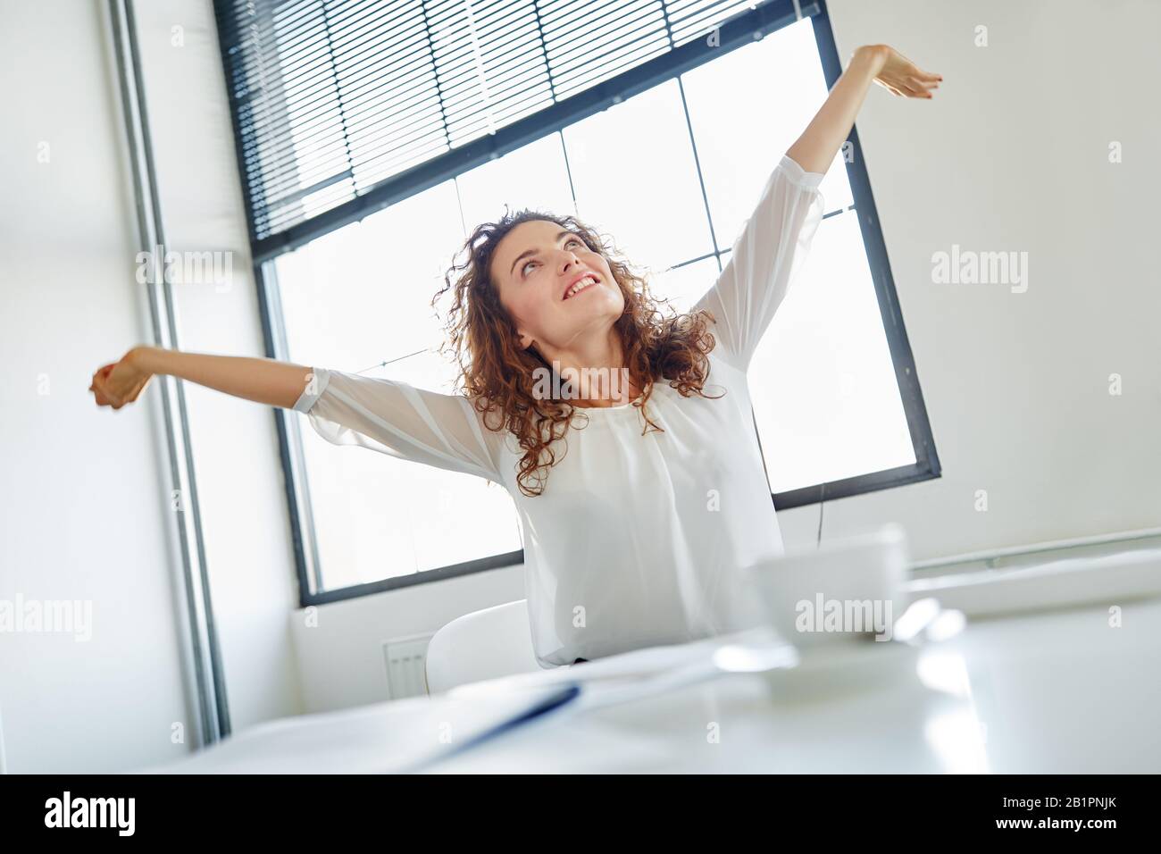 Donna sorridente che fa un esercizio stretching per lei indietro in ufficio Foto Stock