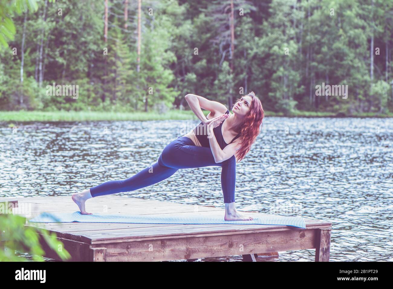 Giovane ragazza yogi praticante yoga, Parsvakonasana, posa ad angolo laterale, sul lago. Concetto di vita sana e di equilibrio naturale Foto Stock