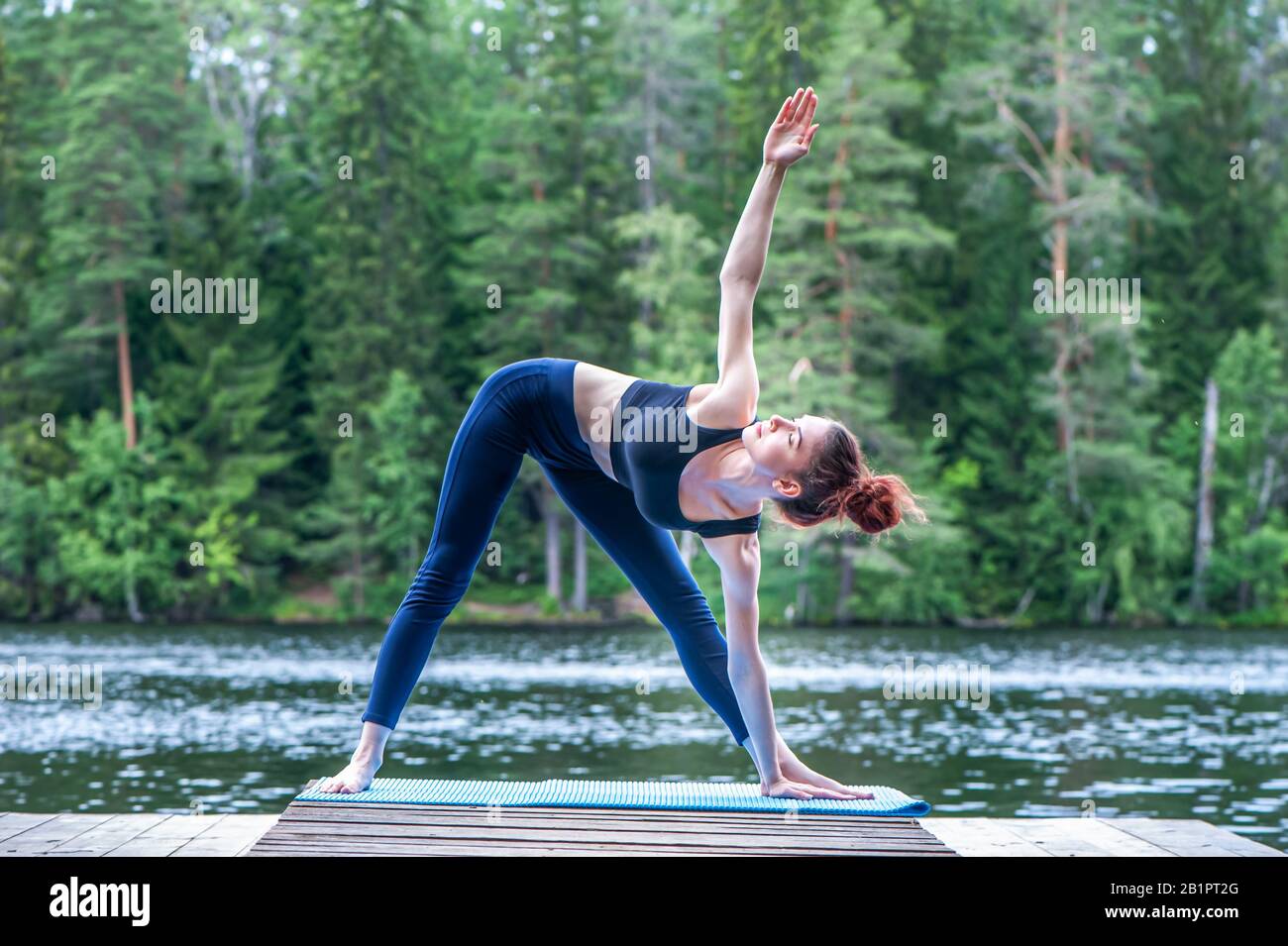 Yogi ragazza che pratica yoga, facendo Utthita Trikonasana esercizio, Extended triangolo posa sul lago. Concetto di vita sana e di equilibrio naturale Foto Stock