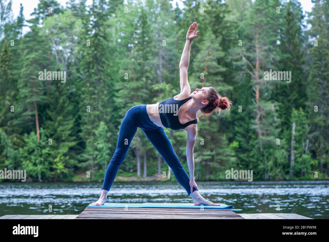 Yogi ragazza che pratica yoga, facendo Utthita Trikonasana esercizio, Extended triangolo posa sul lago. Il concetto di pacificazione, stile di vita sano. Foto Stock