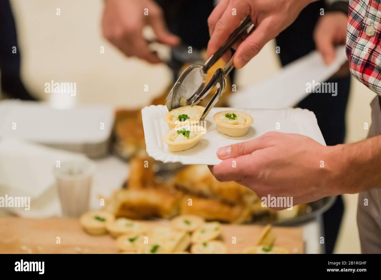 Primo piano di cibo uomo che si scooping utilizzando utensile tong a buffet cibo ristorante catering self service tavolo. Foto Stock