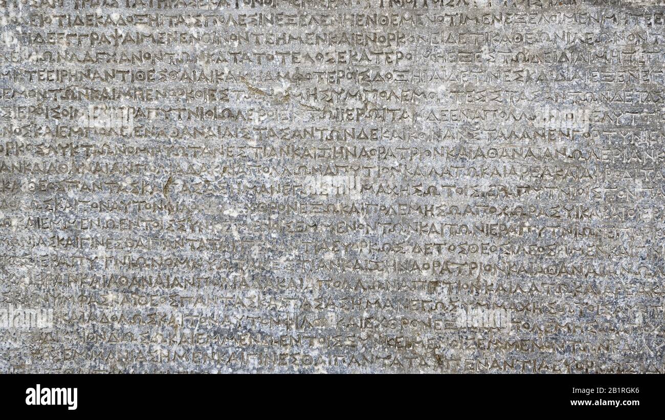 Antica scrittura greca su roccia per sfondo. Antica iscrizione scolpita in pietra. Primo piano del testo del vecchio script. Muro grigio con lettere storiche. Vintage Foto Stock
