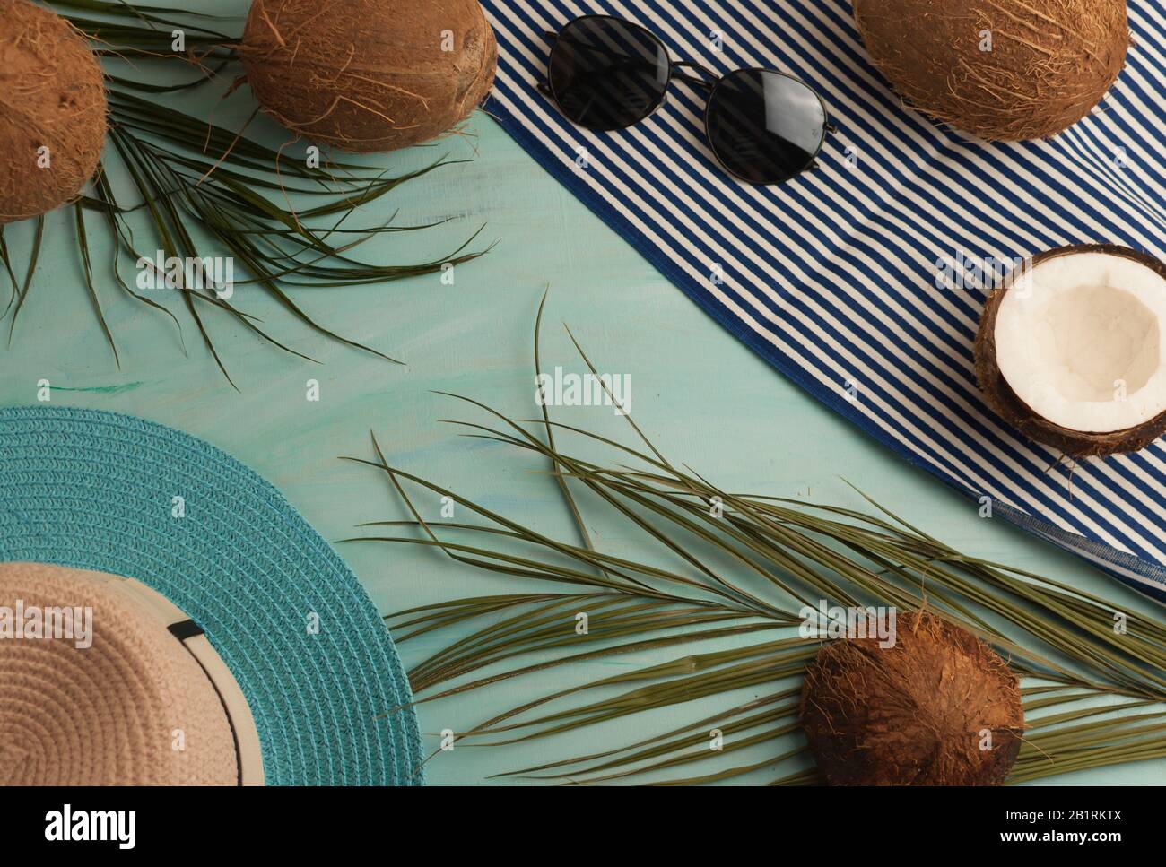 Composizione o layout estivo. Foglie di palma tropicale, cappello, bicchieri, telo mare, cocco su uno sfondo di verde mare. Il concetto della stagione estiva Foto Stock