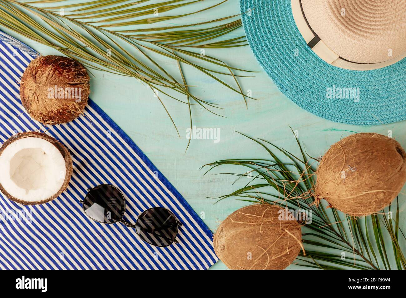 Composizione o layout estivo. Foglie di palma tropicale, cappello, bicchieri, telo mare, cocco su uno sfondo di verde mare. Il concetto della stagione estiva Foto Stock