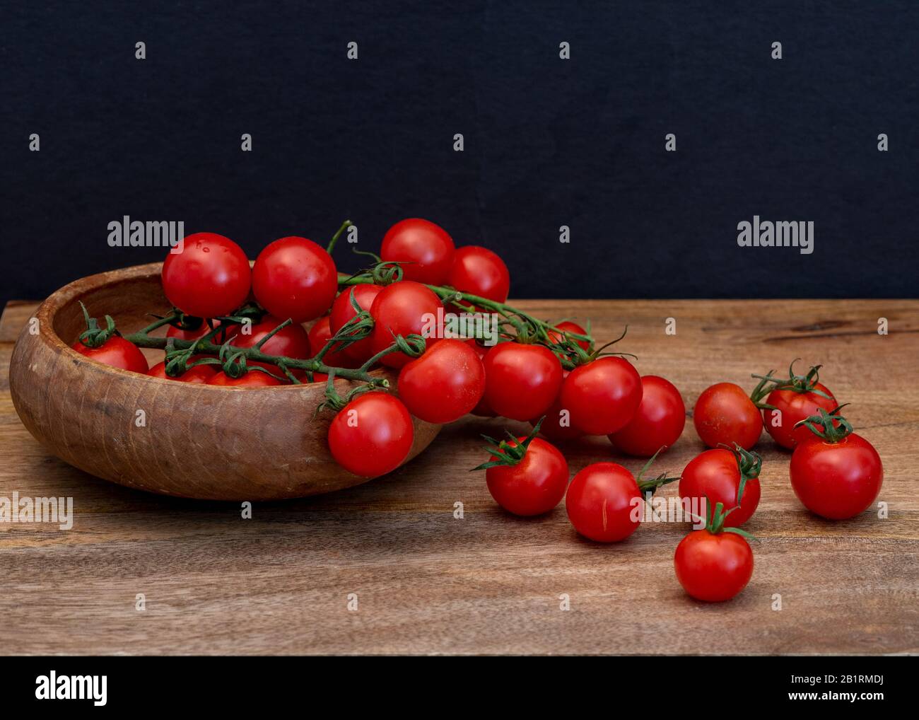 Fresco tomatillos su sfondo nero visto dal lato, su superficie di legno; Fresco intero e tagliato (dimezzato) rosso tomatillos su sfondo nero visto f Foto Stock