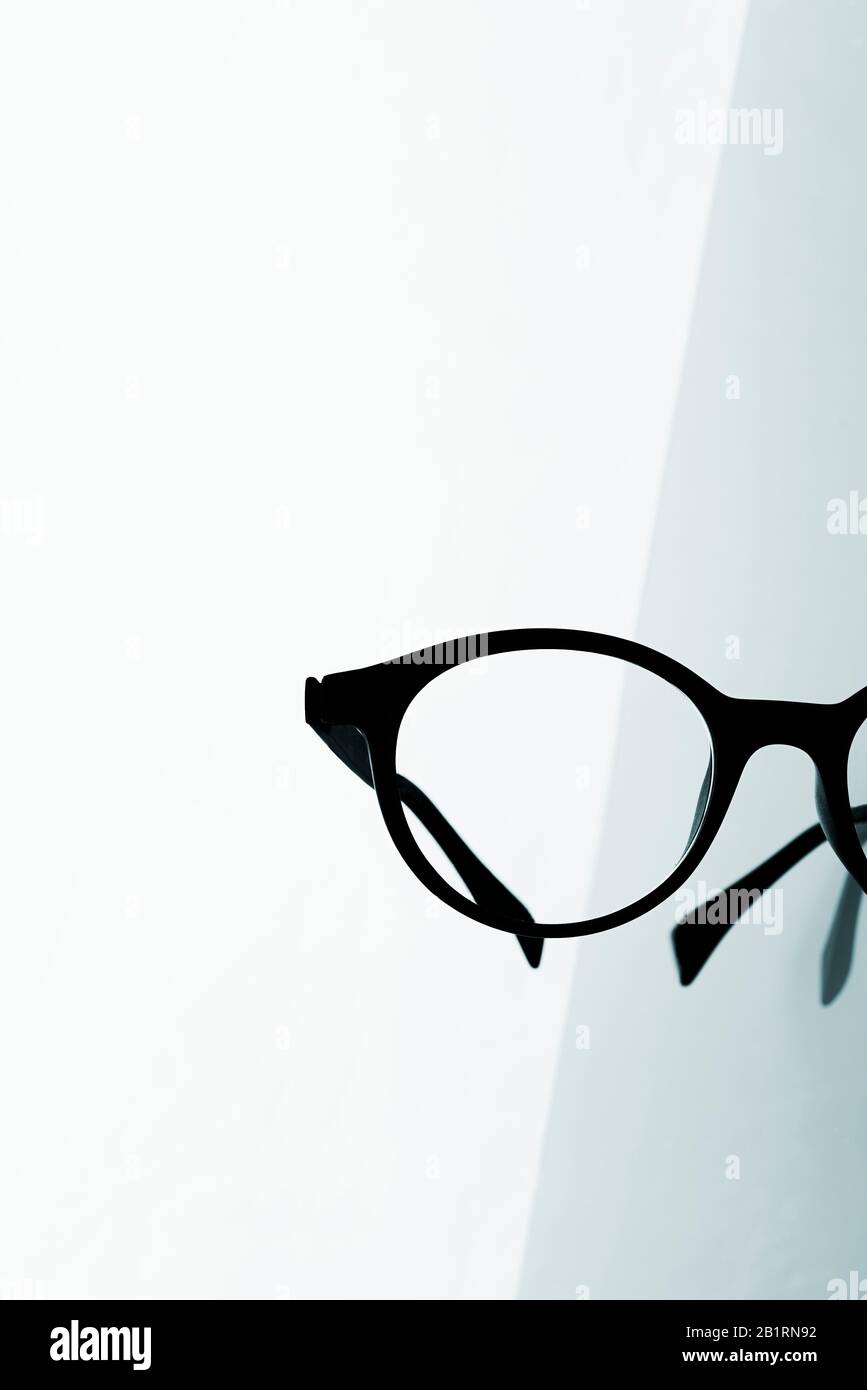primo piano di un paio di occhiali neri su una superficie riflettente su sfondo bianco Foto Stock