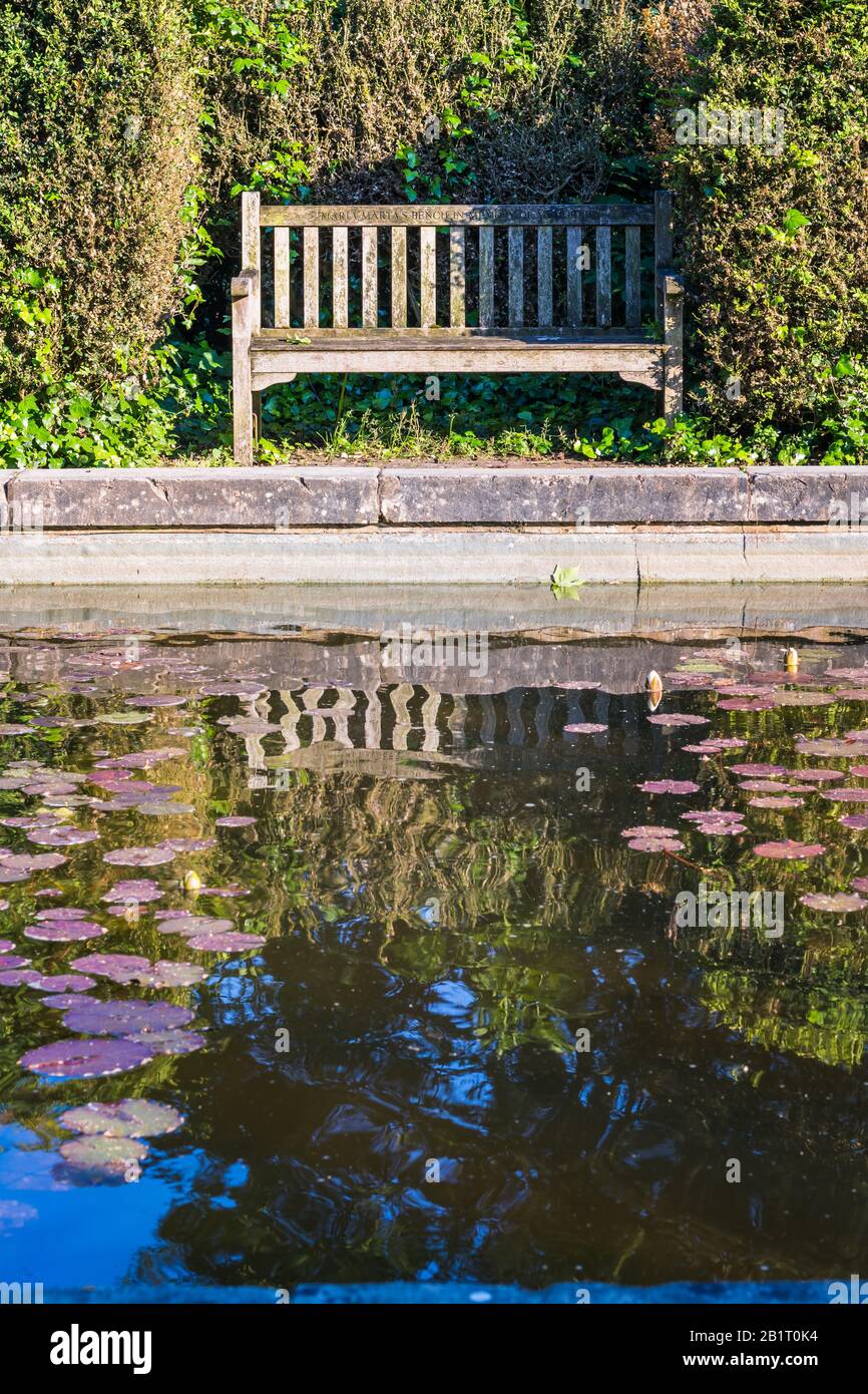 Inglese panca giardino riflesso nel giardino stagno. Preso A Battersea Park, Londra. Foto Stock