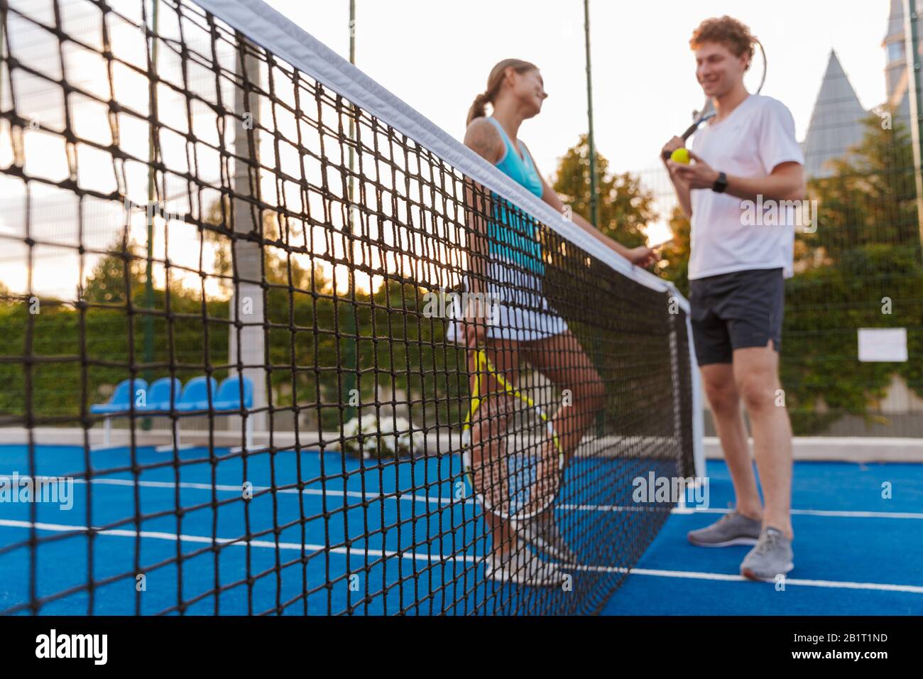 Immagine di un giovane sorridente positivo due giocatori positivi di tennis donna e uomo all'aperto che parlano con l'altro tenendo racchetta. Foto Stock
