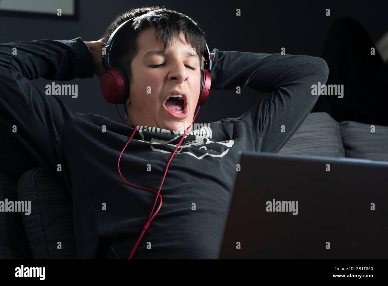 Ragazzo adolescente stanco , 13, yawns come lui guarda i video online sul laptop Foto Stock