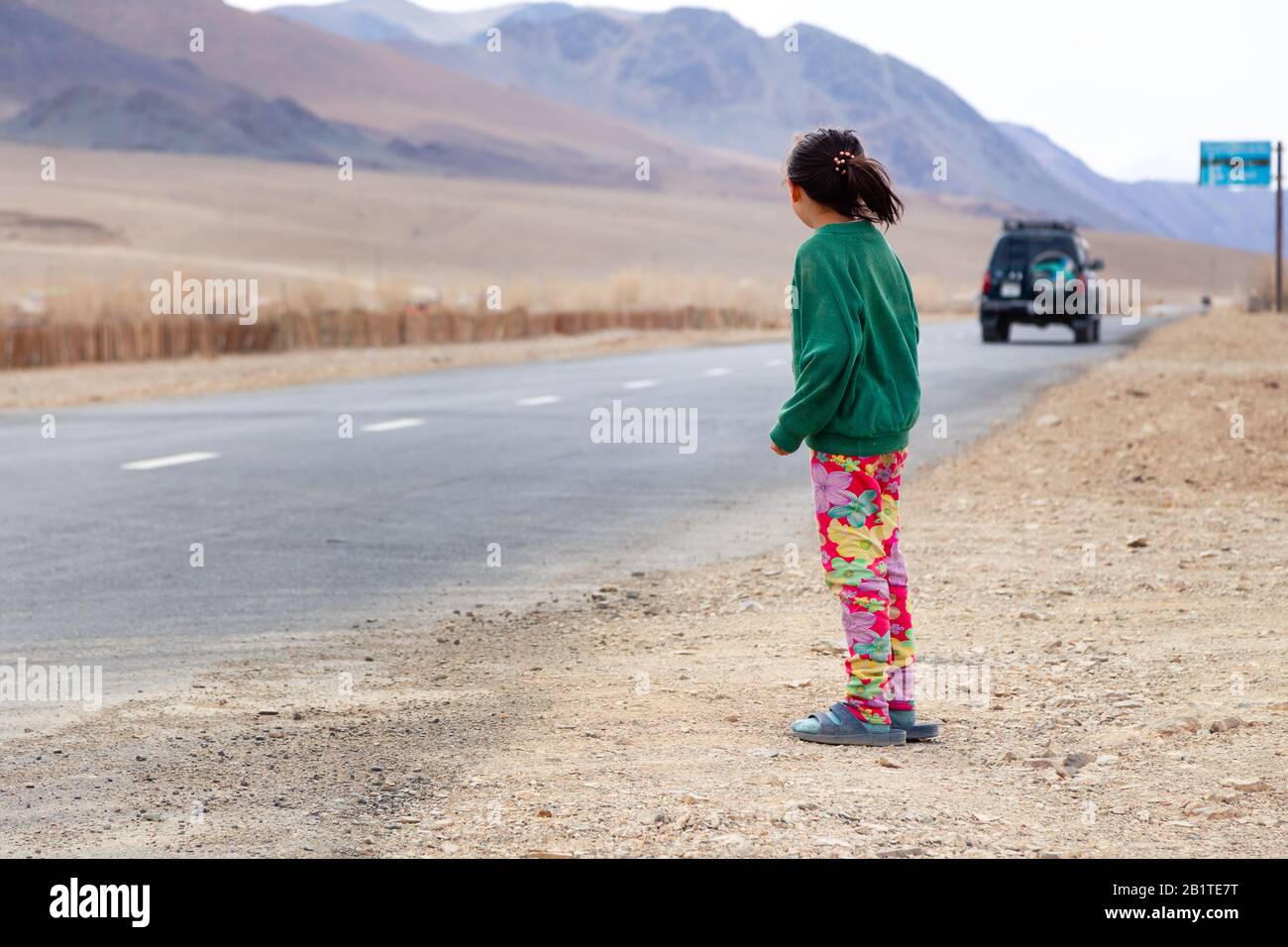 Mongolia Ulgii 2019-05-05 ragazza mongolo in abiti colorati si erge sulla strada e si prende cura della macchina in partenza. Concetto orfano, famiglia adottiva Foto Stock