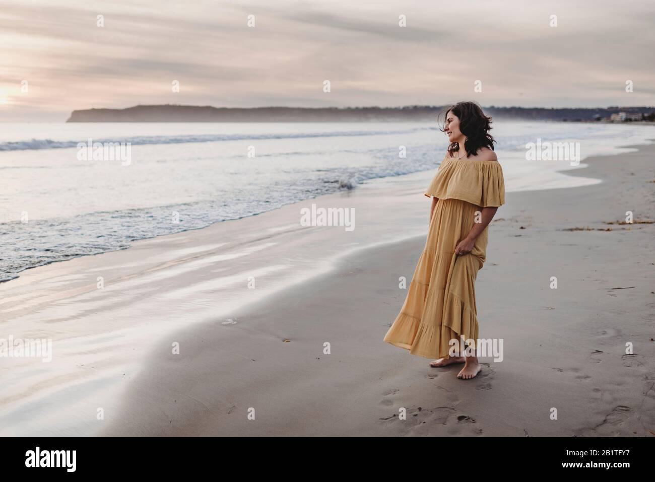 Ritratto lifestyle di giovane donna in piedi sulla spiaggia contro il cielo nuvoloso Foto Stock