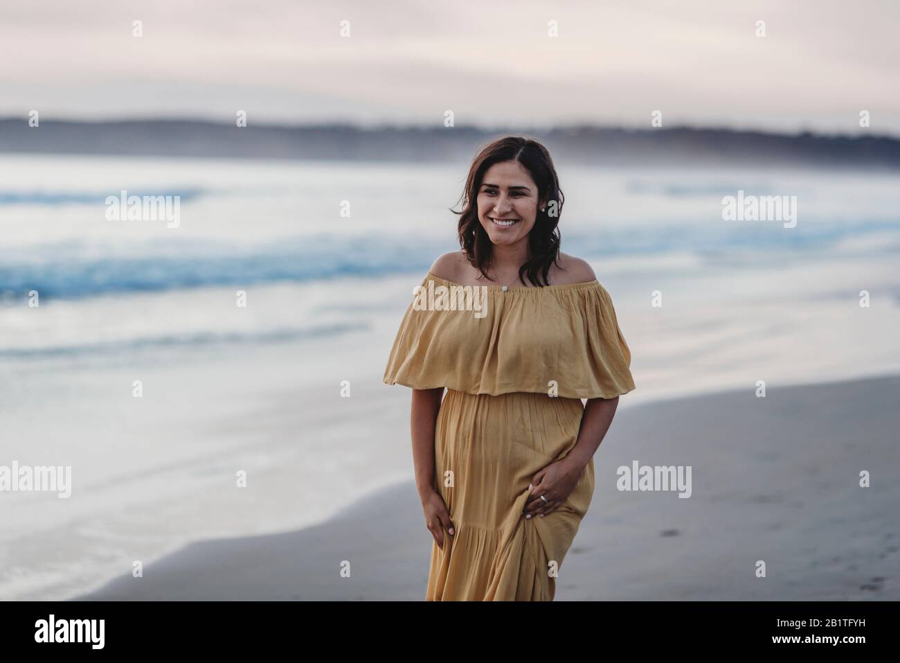 Ritratto lifestyle di giovane donna che cammina sulla spiaggia contro il cielo nuvoloso Foto Stock