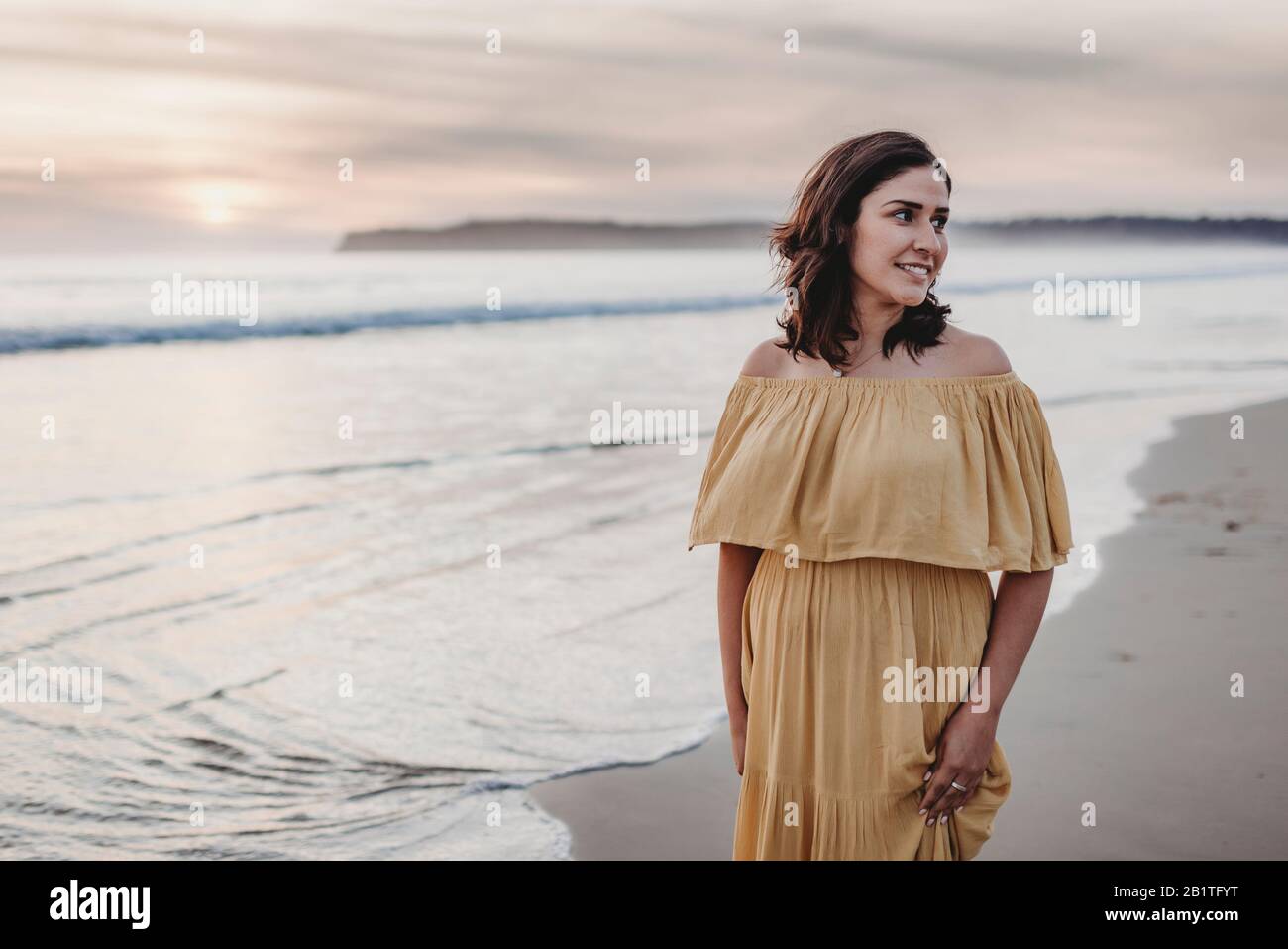 Ritratto lifestyle di giovane donna in piedi sulla spiaggia contro il cielo nuvoloso Foto Stock