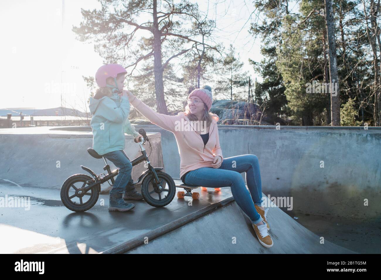 mamma che aiuta sua figlia con il casco in uno skatepark Foto Stock