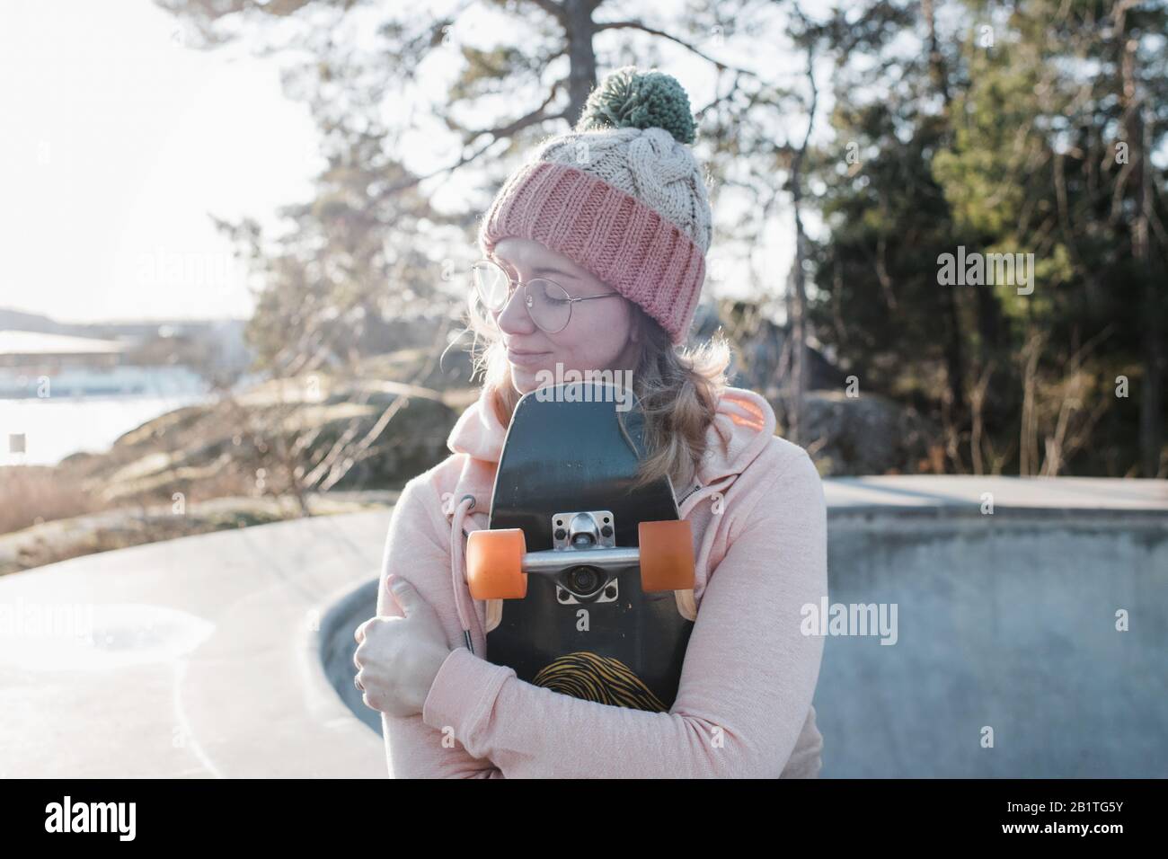 donna sedette con gli occhi chiusi tenendo lo skateboard in uno skatepark Foto Stock