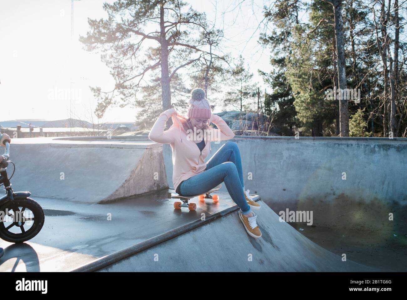 donna sedette su uno skateboard in uno skatepark sorridente al sole Foto Stock