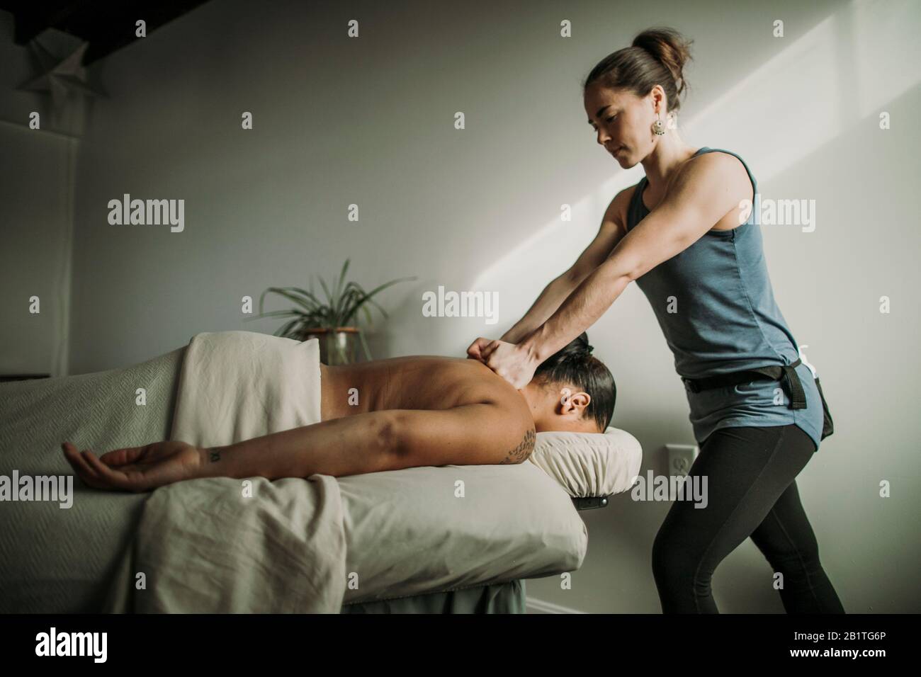 Massaggio femminile terapista massaggi le spalle del paziente afroamericano Foto Stock