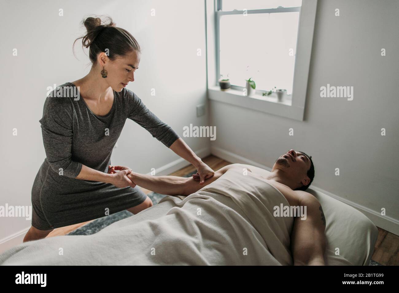 Una terapista massaggiante femminile tratta il bicep di un uomo Foto Stock