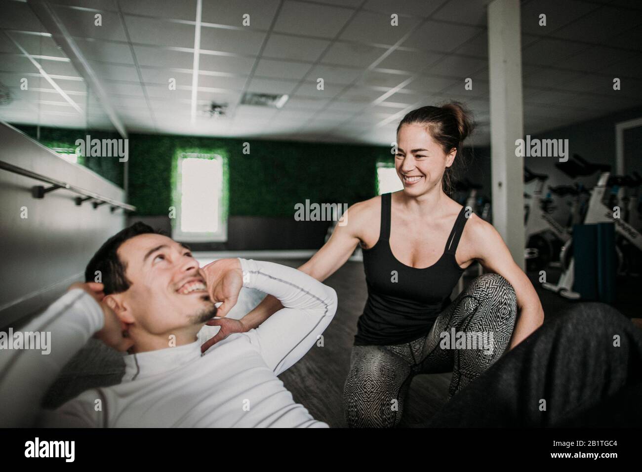 l'addestratore personale femminile ride con il suo cliente maschio mentre lui risolve Foto Stock