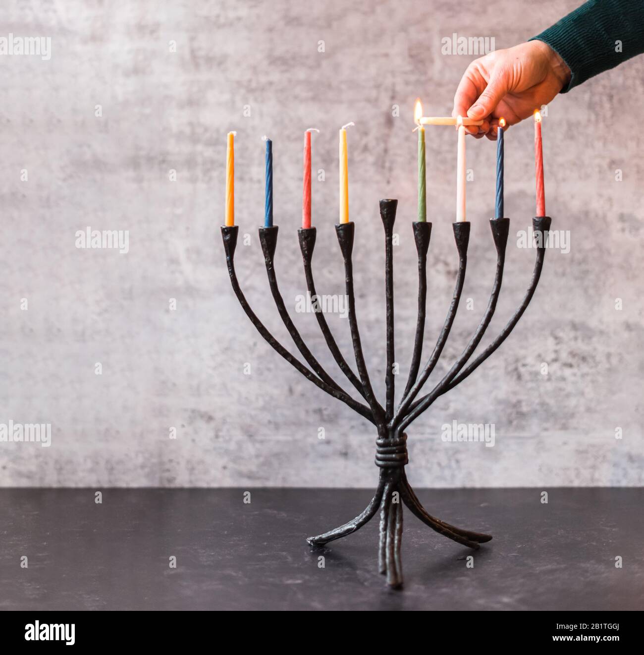 Immagine ritagliata di una mano che illumina candele su menorah per Hanukkah. Foto Stock
