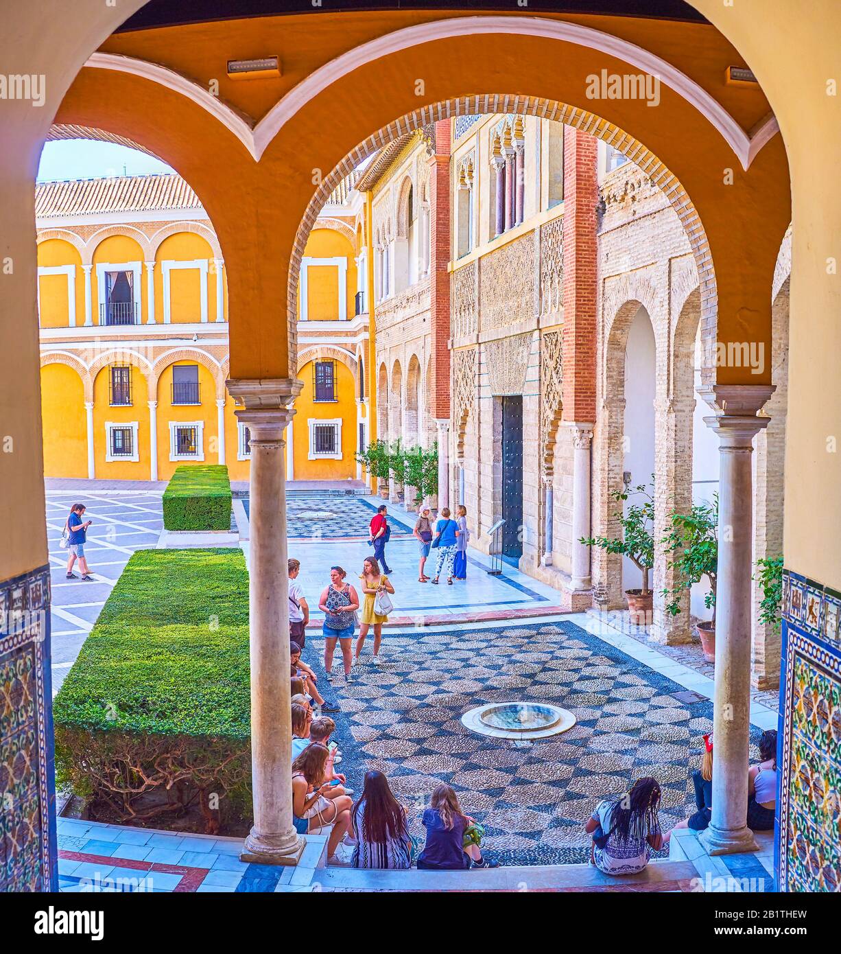 Siviglia, SPAGNA - 1 OTTOBRE 2019: La vista attraverso i portici sul patio de la Monteria del complesso del Palazzo reale Alcazar e adolescenti seduti sulla sta Foto Stock