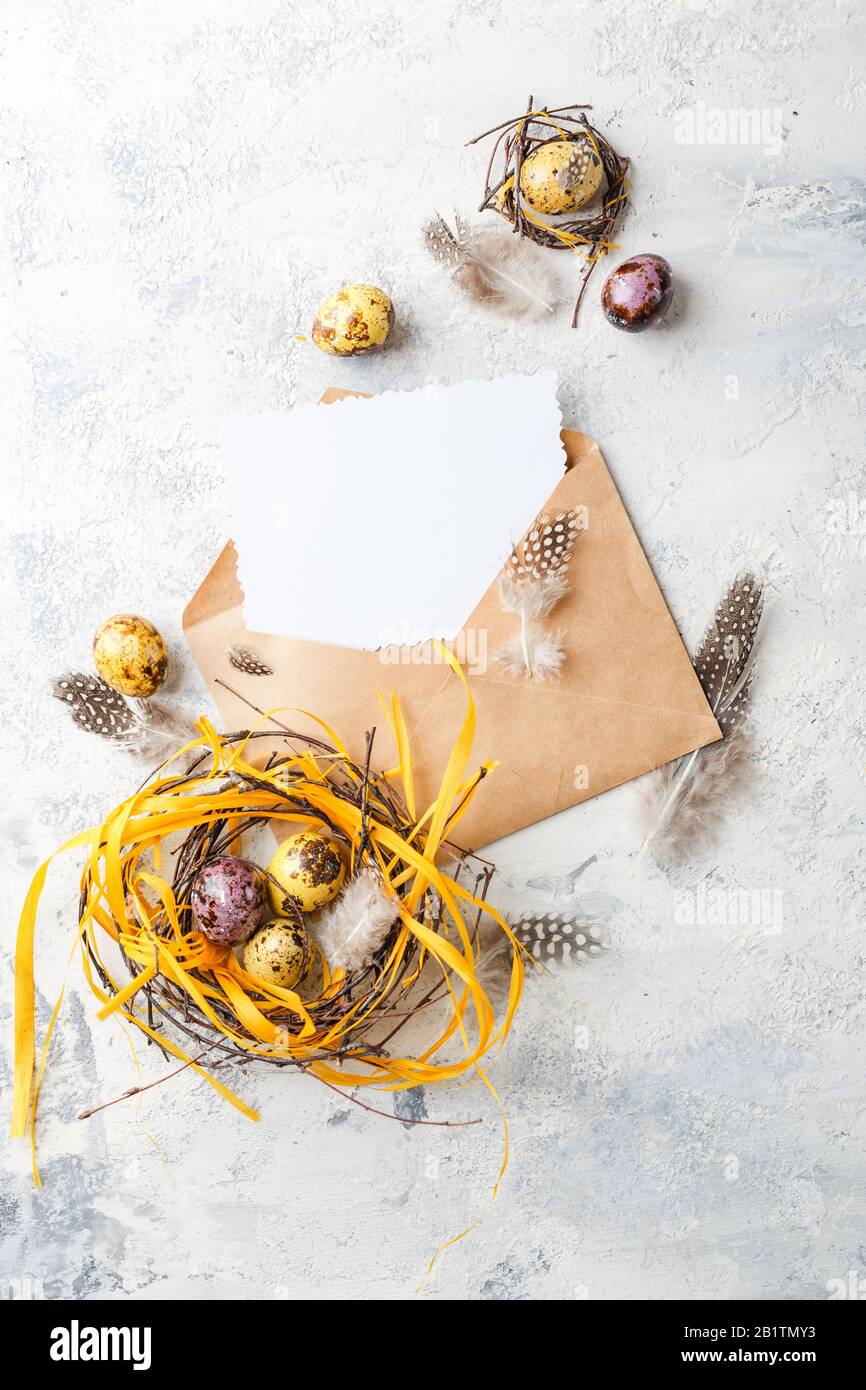 Uova di quaglia di Pasqua di colore giallo e viola con piume in piccoli nidi e carta di auguri in involucro. Profondità di campo bassa. Vista dall'alto. Spazio per te Foto Stock